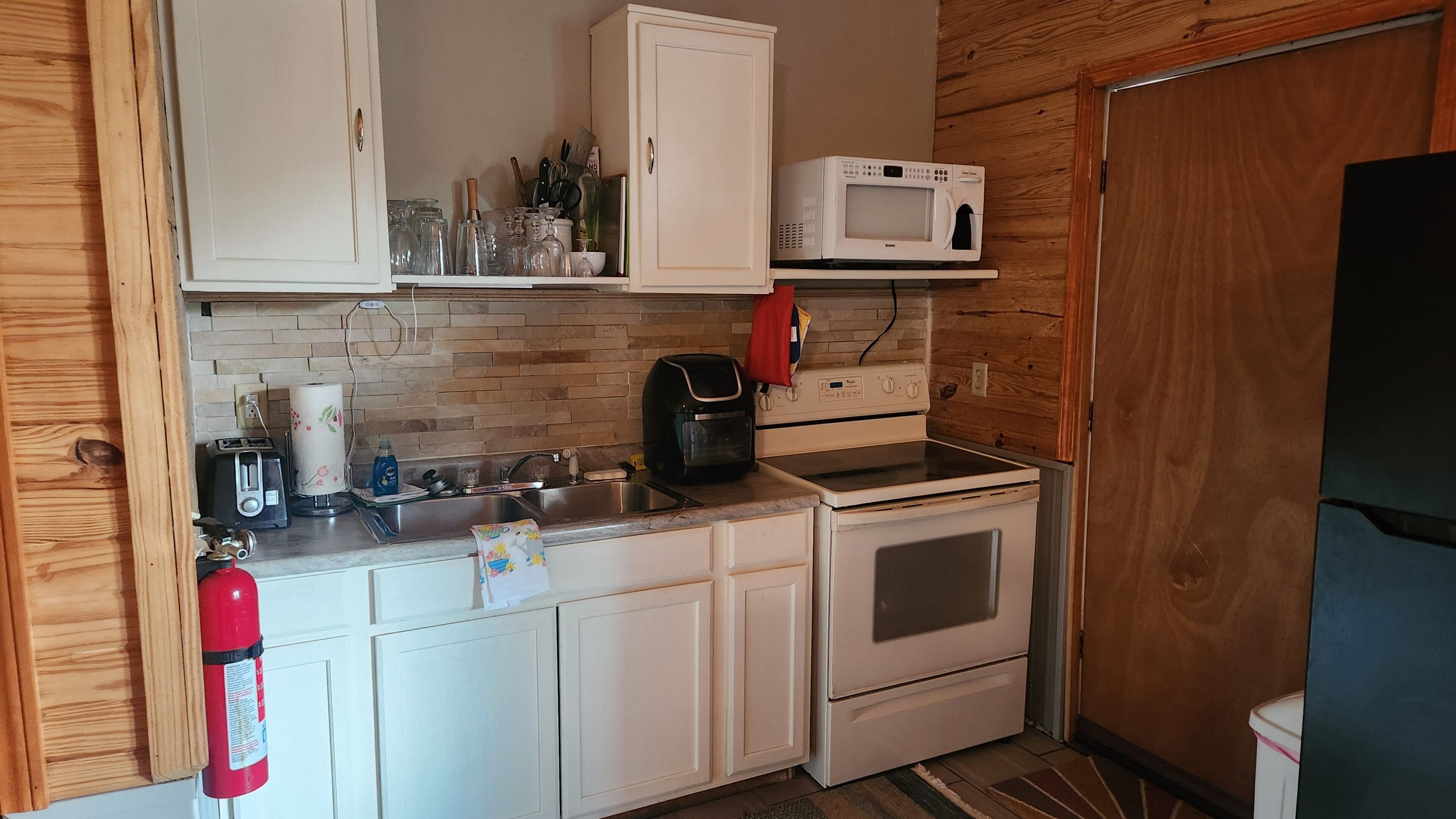 Una cocina compacta con armarios blancos, un microondas, un tostador y un lavabo.