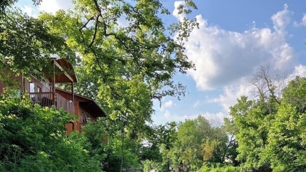 A riverside view with a wooden cabin and lush greenery. - Cabin on the Water! Cabin #5 (Noel)