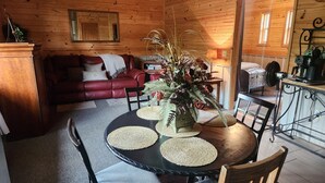 A wooden cabin interior with a dining table, chairs, a red leather sofa, a mirror, and a kitchen area with a coffee machine. - Cabin on the Water! Cabin #5 (Noel)