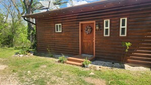 A wooden cabin with a front door, two windows, a satellite dish, and a small porch area. - Cabin on the Water! Cabin #5 (Noel)