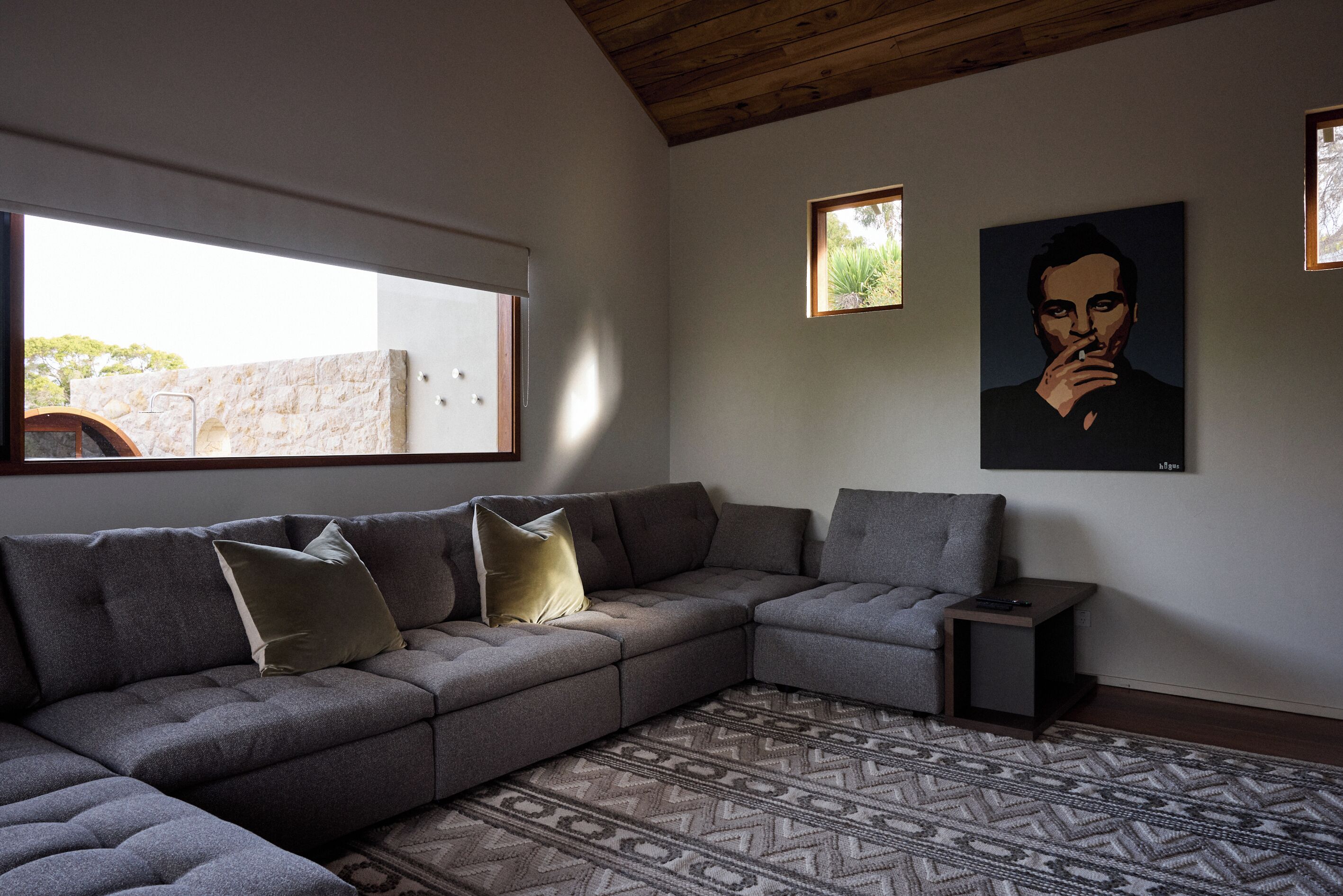 Ein modernes Wohnzimmer mit einem grauen Ecksofa, einem gemusterten Teppich und einem Bild an der Wand.