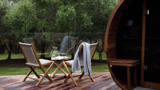 A wooden deck with two chairs and a table, a glass railing, and a large wooden barrel structure.