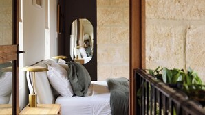 A bedroom with a bed, bedside lamps, a mirror, and a view of a stone wall.
