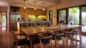A modern kitchen with wooden cabinets, a central island, and a dining area with a large wooden table and chairs.