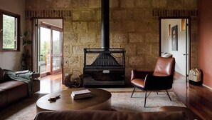 A cozy living room with a stone wall, a fireplace, leather furniture, and a view through a glass door.