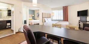 Een hotelkamer met een eethoek, een bed, een televisie en een badkamer die door een open deur zichtbaar is.