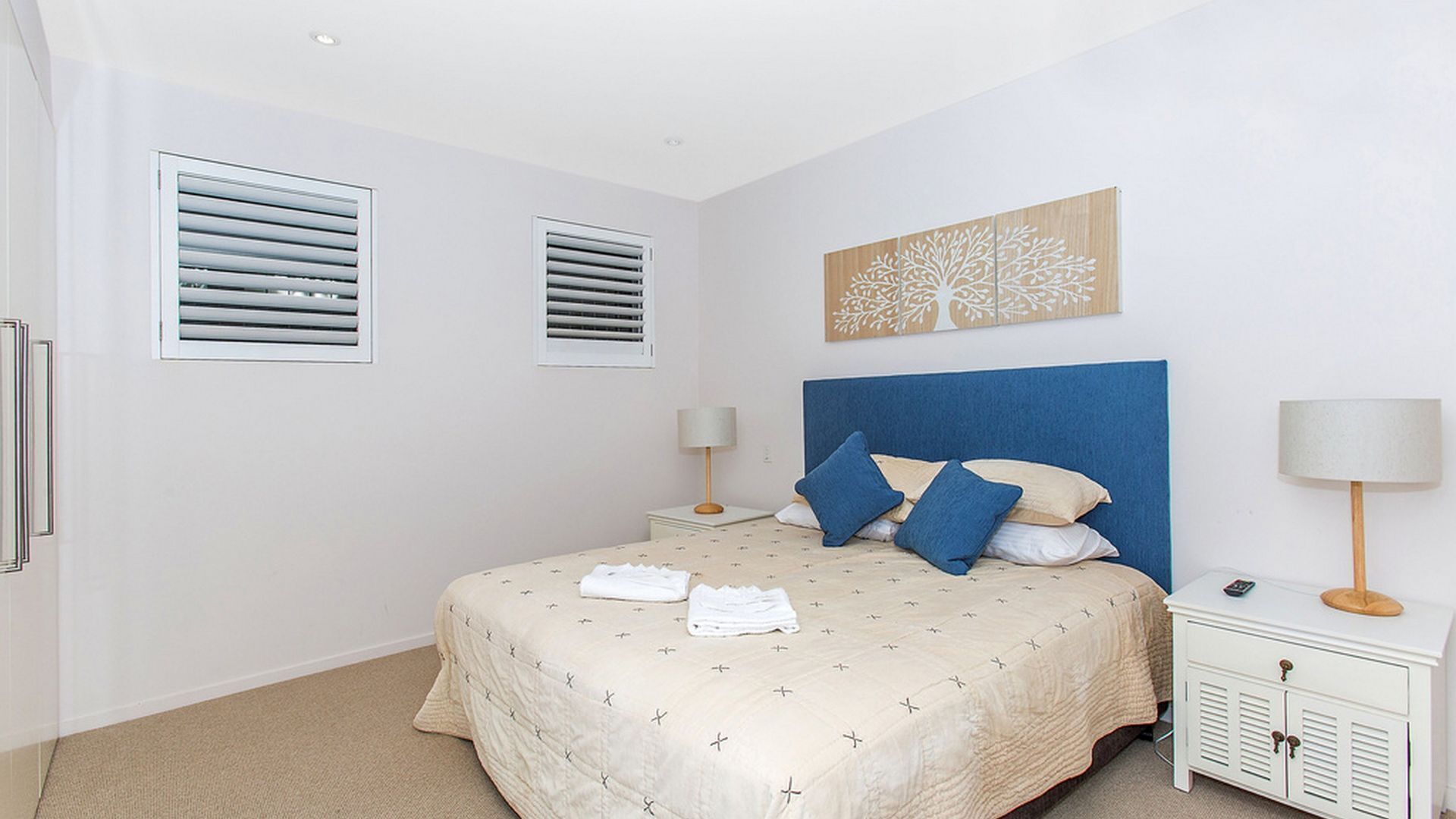 Une chambre à coucher comprenant un lit, deux tables de chevet, une commode, une œuvre d’art accrochée au mur et une fenêtre avec des stores.
