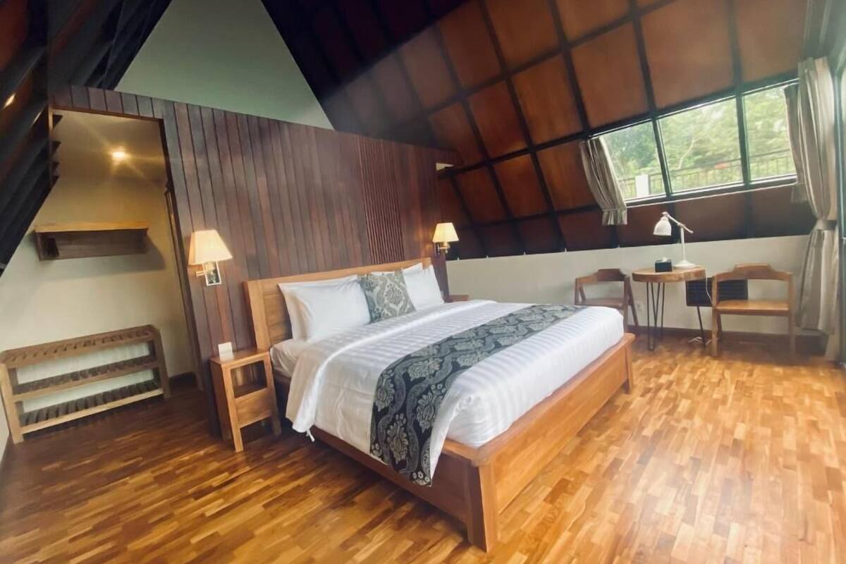 A bedroom with a wooden bed, bedside tables, a desk, and a chair.