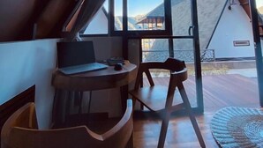 Um interior moderno com teto inclinado, janelas amplas, uma mesa de madeira e uma cadeira.