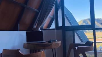 Ein Zimmer mit schrägen Wänden, einem großen Fenster mit Blick ins Grüne und zwei Holzstühlen mit einem Laptop auf einem kleinen Tisch.