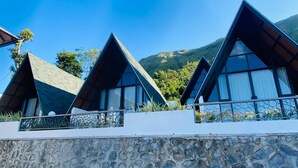 Uma fileira de cabanas modernas com telhados triangulares e grandes janelas, com montanhas ao fundo.