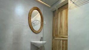 Casa de banho moderna com divisória de vidro, porta de madeira, lavatório branco e espelho.