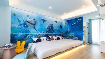 Un dormitorio con un gran mural de criaturas marinas en la pared, una cama con ropa blanca, una mesita con una tetera y una silla.