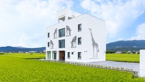 A modern white building with large windows and a flat roof, surrounded by green fields and mountains in the background. - New Wunuanzoo (Jiaoxi)