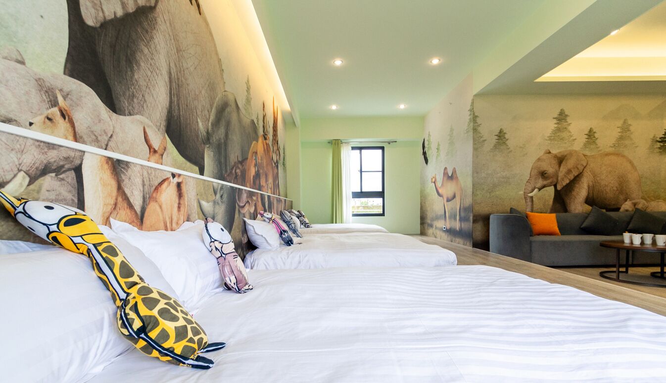 Une chambre d’hôtel avec une grande fresque représentant des animaux, un canapé et un lit agrémenté d’oreillers à motifs de girafes.