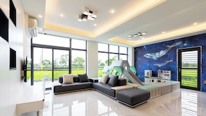 A modern living room with a sectional sofa, a flat-screen TV, and a mural of space. - New Wunuanzoo (Jiaoxi)