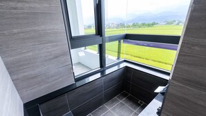 A modern bathroom with dark tiles, a window with a view of a green field and mountains, and a black bathtub. - New Wunuanzoo (Jiaoxi)