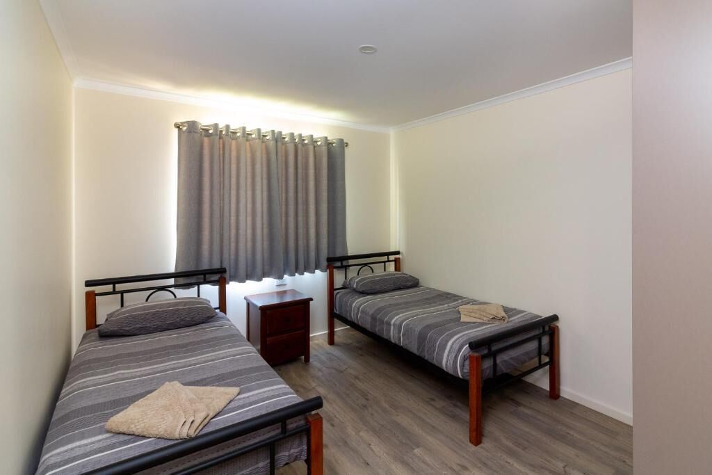 Una habitación pequeña con dos camas individuales, una mesita de noche y una ventana con cortinas.