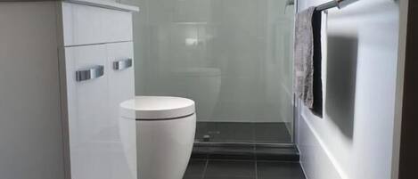 Un baño moderno con inodoro blanco, cabina de ducha de vidrio y mueble blanco con pomos plateados.
