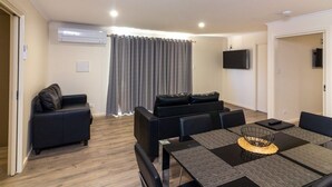 A modern living room with a sofa set, a dining table with placemats, and a flat-screen TV mounted on the wall. - Paringa Caravan Park (Paringa)