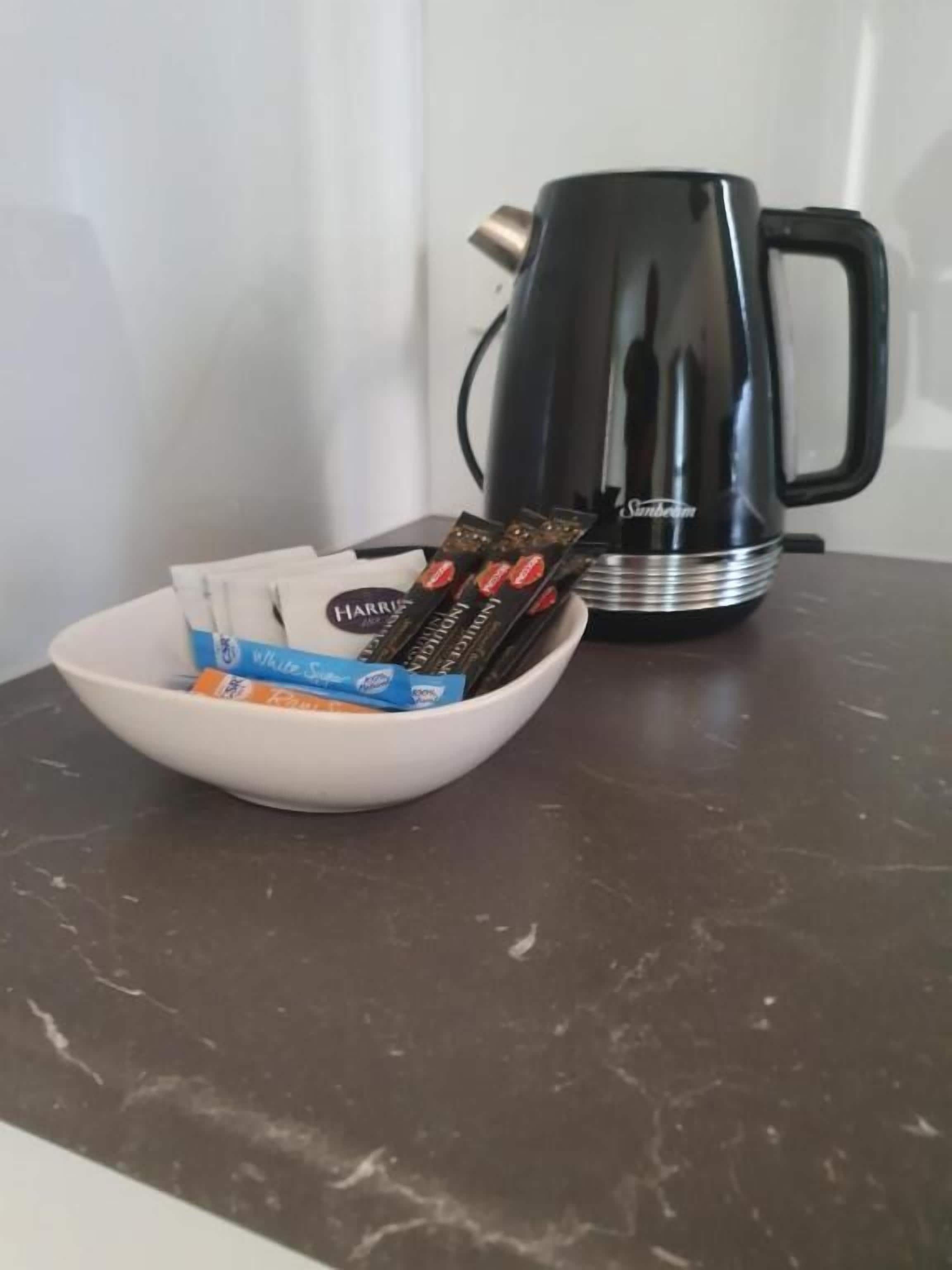 Un tazón blanco con barras de chocolate y una cafetera negra sobre una encimera oscura.