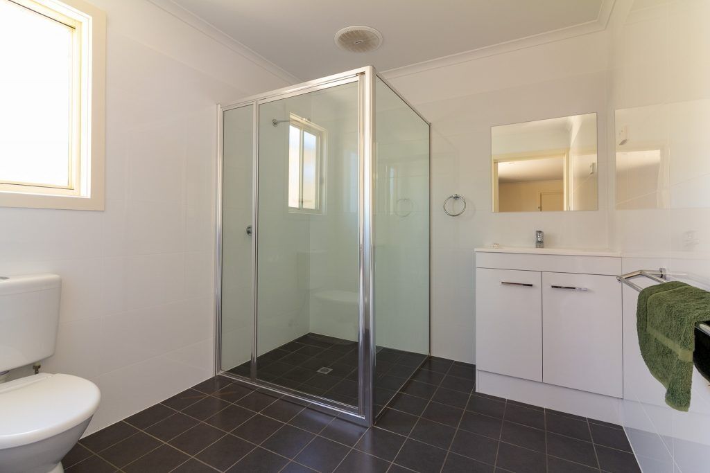 Un baño con cabina de ducha de vidrio, inodoro blanco, lavabo con espejo y un perchero para toallas.
