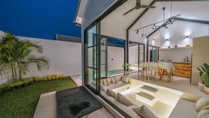 A modern house with a glass-enclosed patio, a pool, and a dining area with a table and chairs. - Villa Cha Cha  (Canggu)