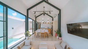 A modern interior with a dining area, kitchen, and seating area with large windows. - Villa Cha Cha  (Canggu)