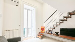 A modern living room with a grey sofa, a staircase with a minimalist design, and a flat-screen TV on a wooden console. - Studio Duplex at National Museum (Naples)