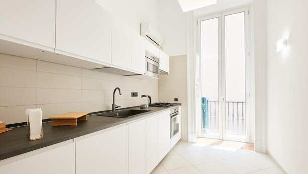 A modern kitchen with white cabinets, a black countertop, a built-in oven, and a large window with a view of the city. - Studio Duplex at National Museum (Naples)