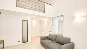 A modern, well-lit hallway with a grey sofa, a large mirror, and a door leading to another room. - Studio Duplex at National Museum (Naples)