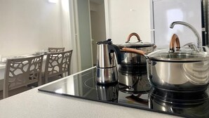 A modern kitchen with a black induction cooktop, stainless steel pots, and a kettle. There is a dining area with a table and chairs in the background. - Grandma Lucia's house (Monopoli)