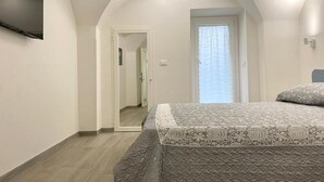 A bedroom with a bed, a television on the wall, a door leading to another room, and a window with curtains. - Grandma Lucia's house (Monopoli)