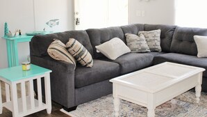 Un salon avec un canapé gris, une table basse blanche et une table d’appoint turquoise.