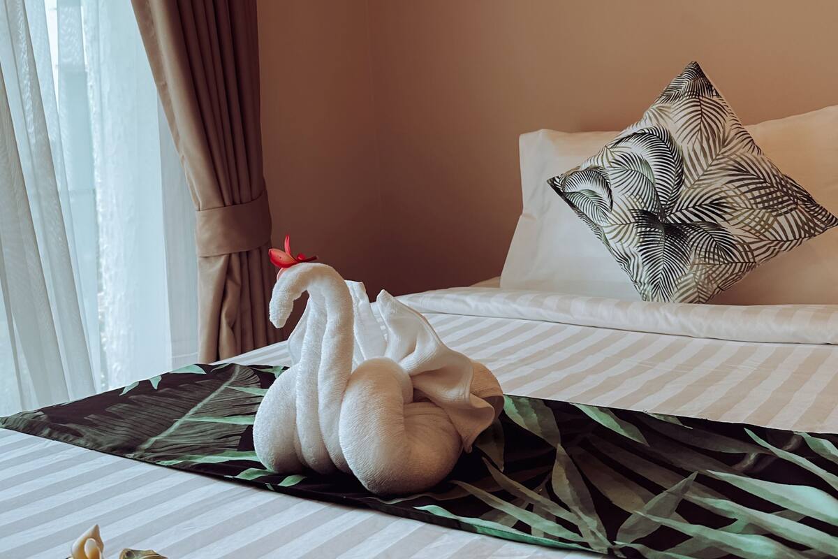 A hotel room with a bed, a decorative wall panel, and a hanging light fixture.