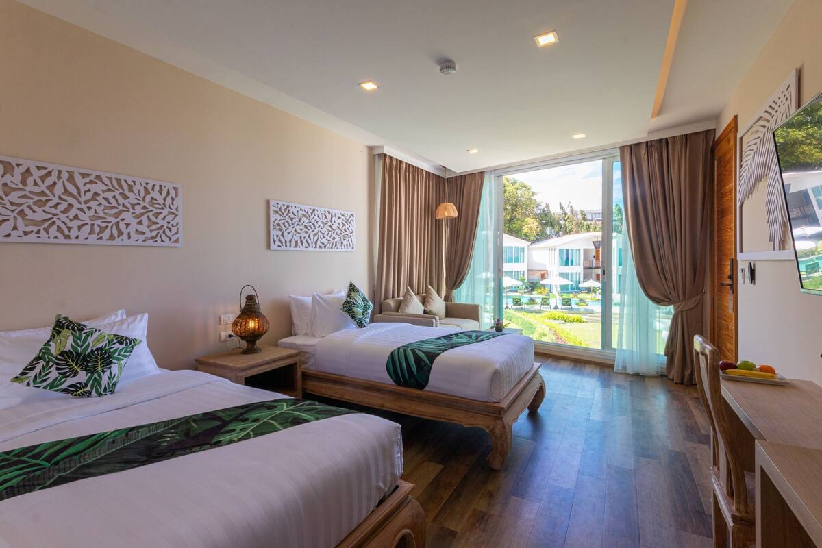 A hotel room with two beds, a dining table, and a large window with curtains.