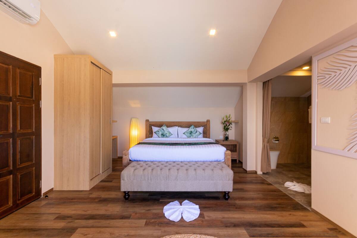 A bedroom with a large bed, wooden wardrobe, and a wooden floor.