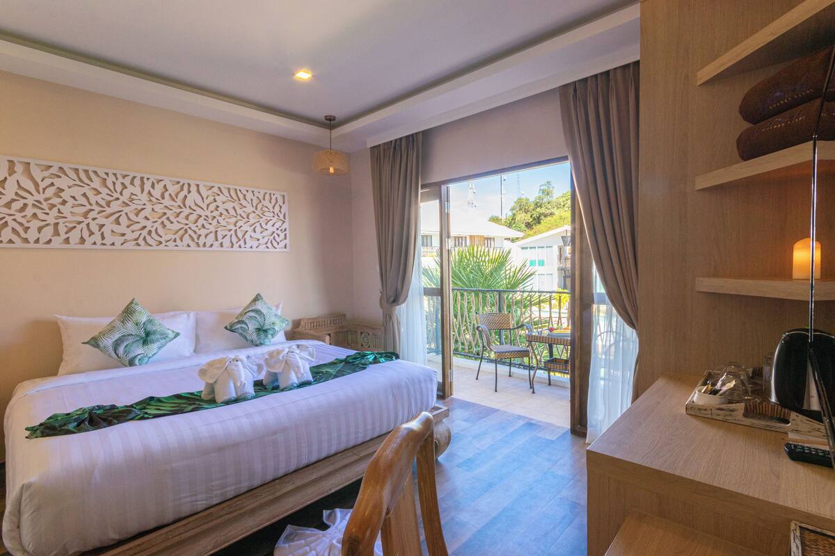 A hotel room with a bed, a desk, a chair, a balcony with a view, and a decorative wall panel.