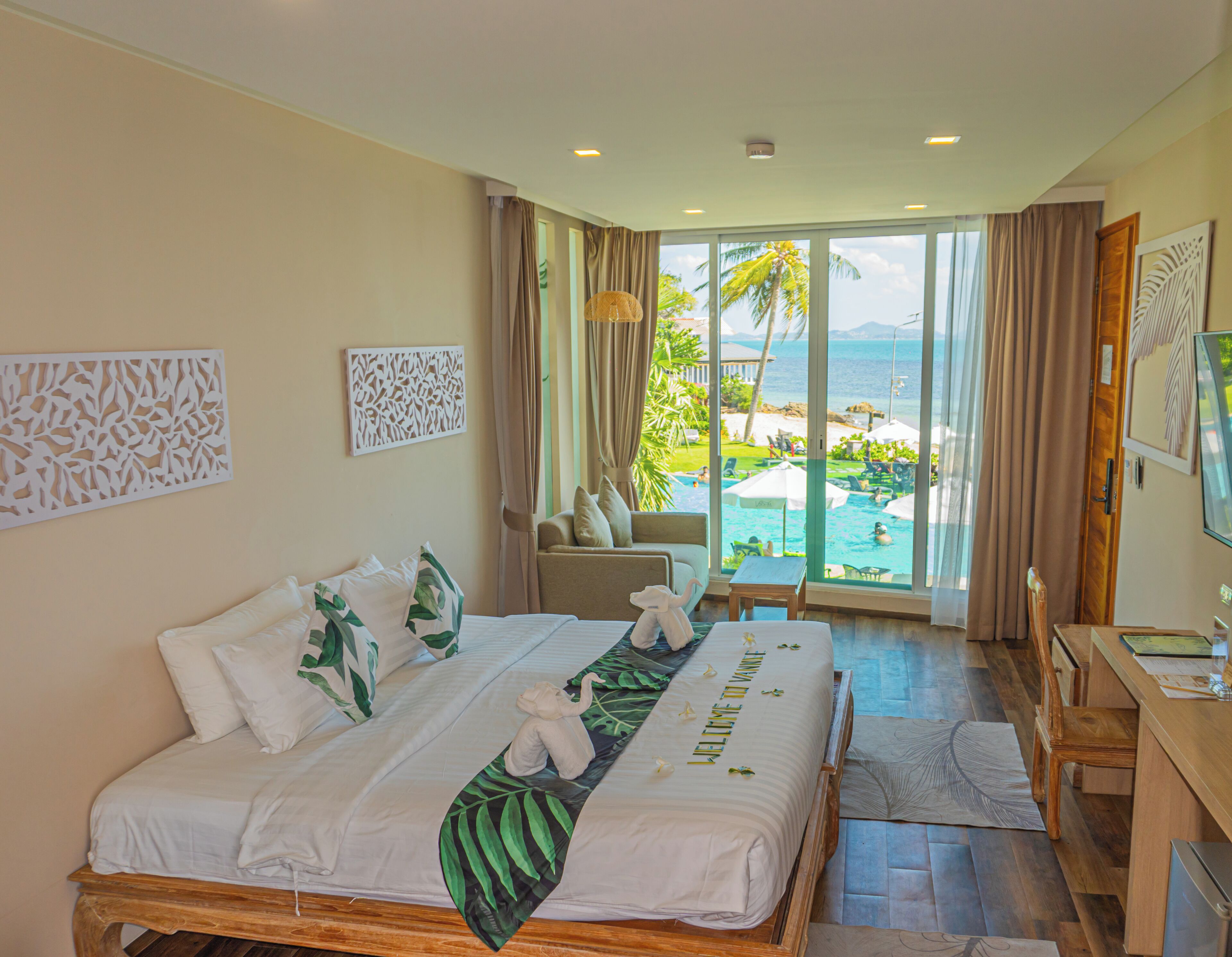 Habitación de hotel con cama, escritorio, silla y vista a una piscina y palmeras.