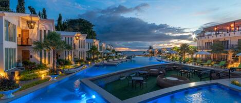 A resort with a large swimming pool, outdoor seating areas, and modern buildings with balconies.