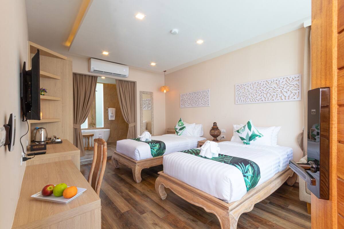A hotel room with two beds, a desk with a fruit plate, a TV, and a wooden cabinet.
