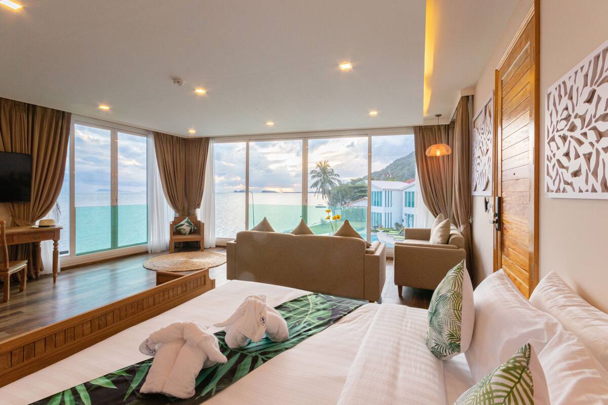 A hotel room with a large bed, a sofa, a desk, and a view of the sea.