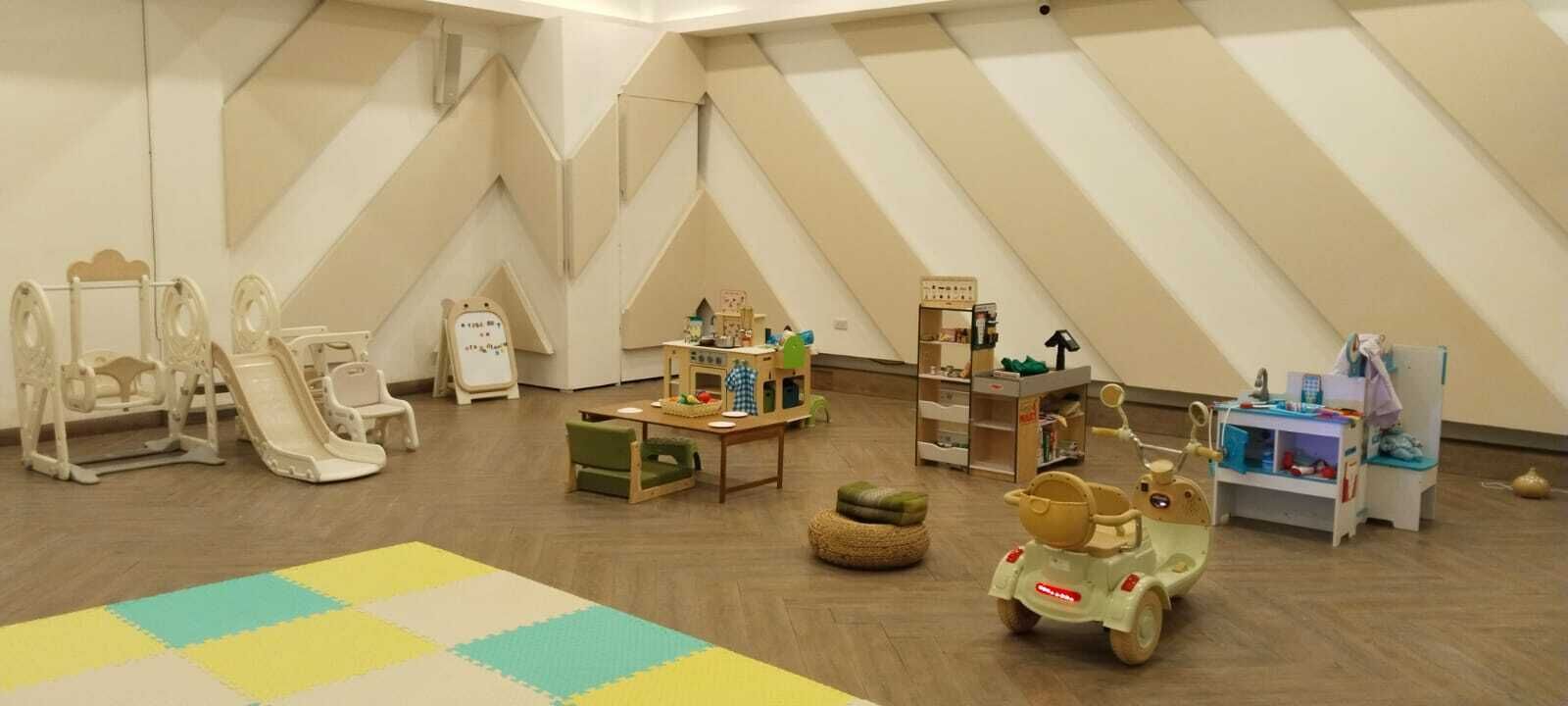Una sala de juegos para niños con techo alto, mesas de juego de madera y diversos juguetes.