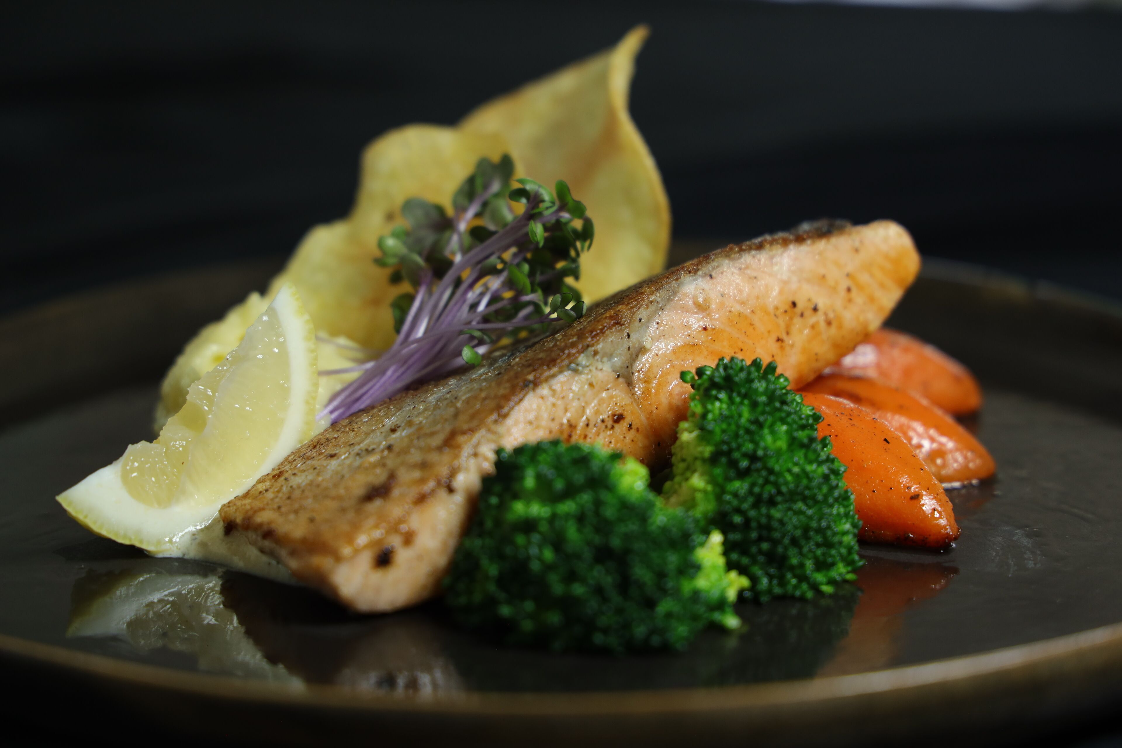 A plate with grilled fish, lemon, broccoli, carrots, and a garnish.