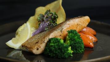 A plate with grilled fish, lemon, broccoli, carrots, and a garnish.