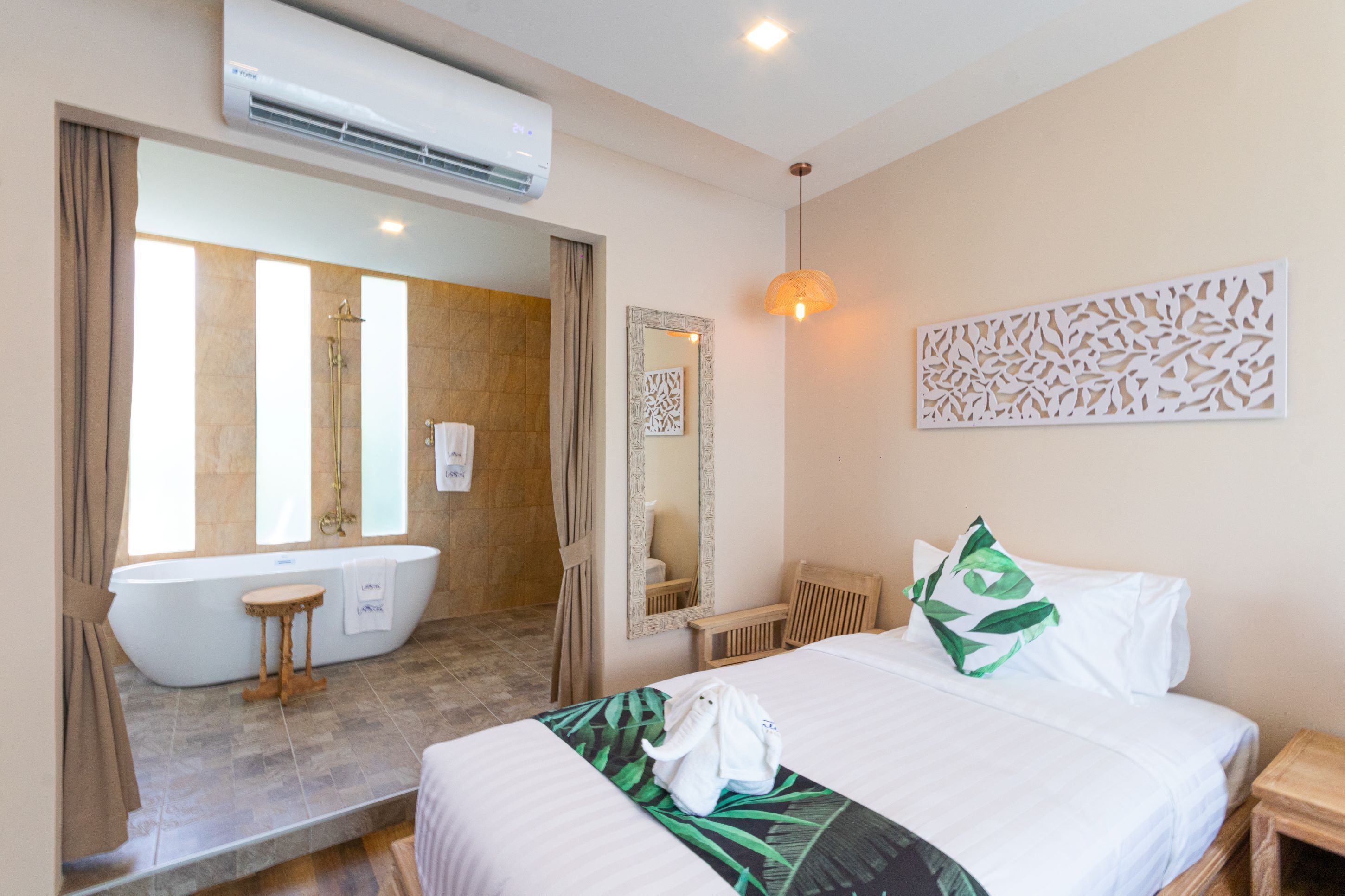 Ein Hotelzimmer mit einem großen Bett, einer Badewanne, einem Holzstuhl, einem kleinen Tisch und einer Wand-Klimaanlage.