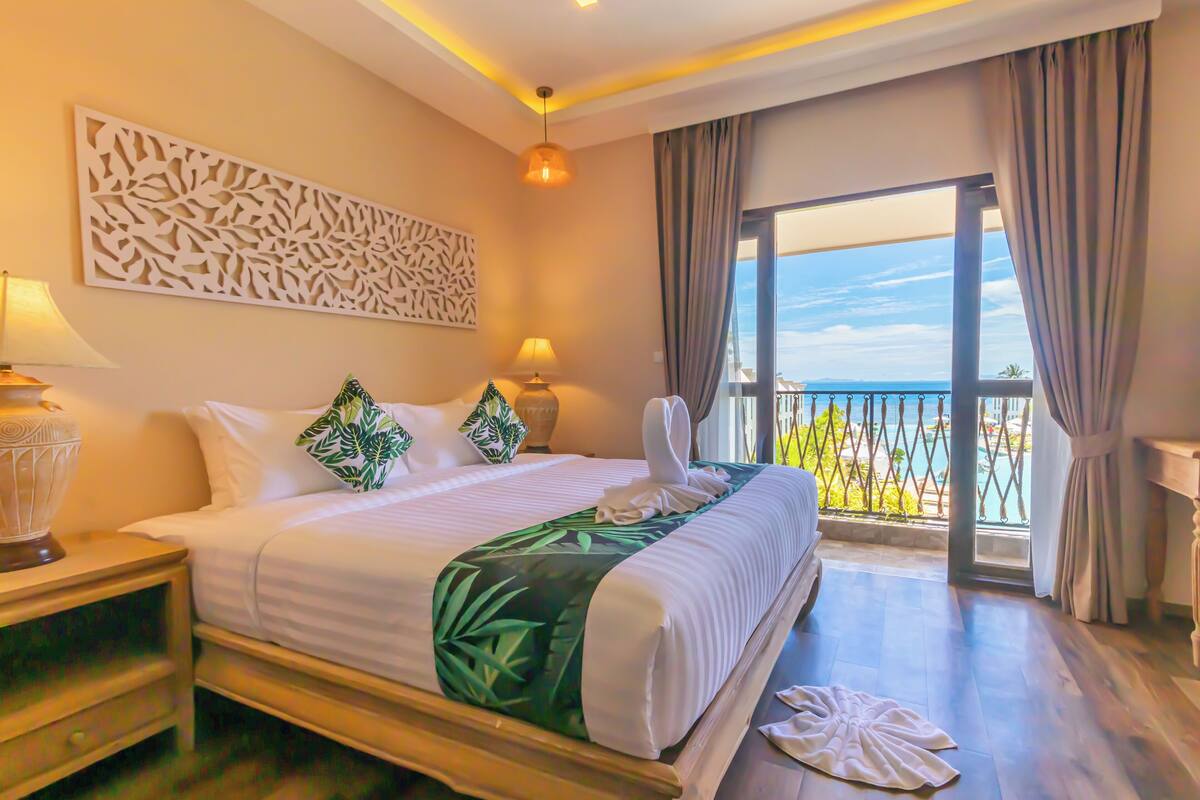 A hotel room with a bed, two bedside lamps, a decorative wall panel, and a balcony with a view.