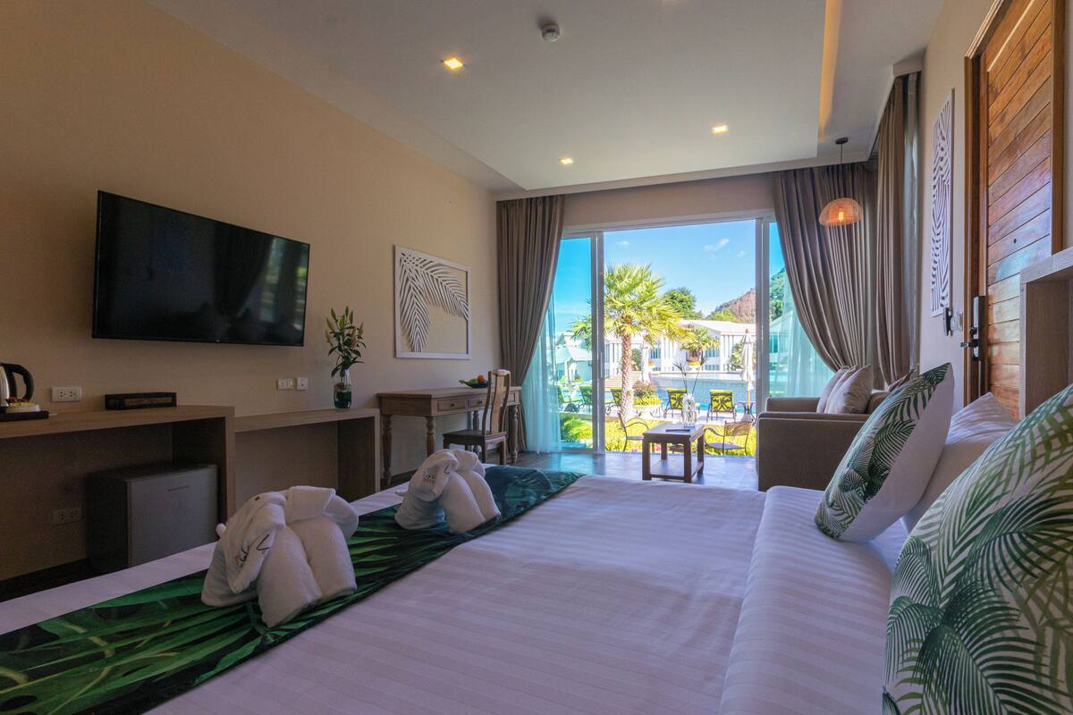 A hotel room with a large bed, a flat-screen TV, a desk, and a view of the outdoor area.