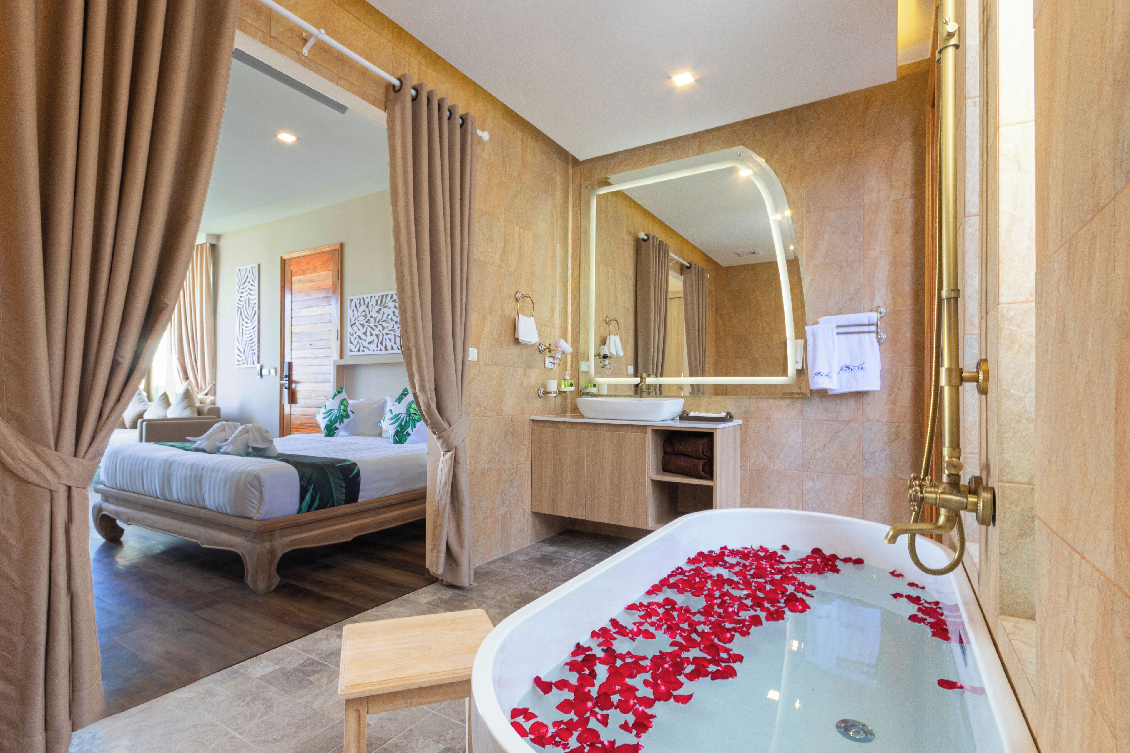 A modern bathroom with a bathtub filled with rose petals, a large mirror, and a wooden vanity.