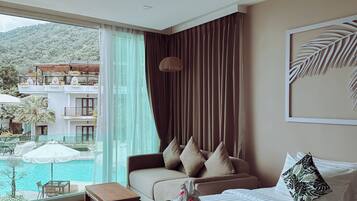 A hotel room with a bed, a view of a pool and building, and a ceiling light.